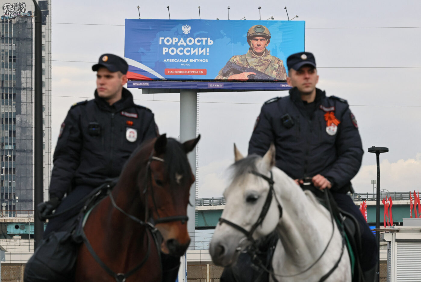 Mounted police patrol a street near a military contract service recruitment banner in Moscow